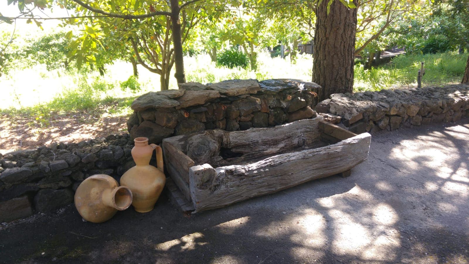 Dornajo, artesa tallada en un tronco de madera ahuecado, apoyada en un muro de piedra junto a cántaros de barro